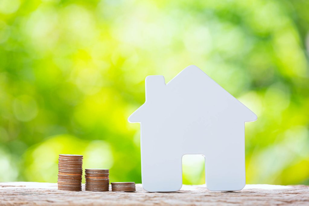 Modell eines Hauses neben Münzen, das das Thema Baufinanzierung symbolisieren soll