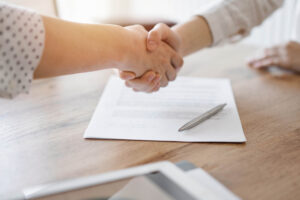 Zwei Menschen schütteln sich die Hand über einem Immobilienkaufvertrag 
