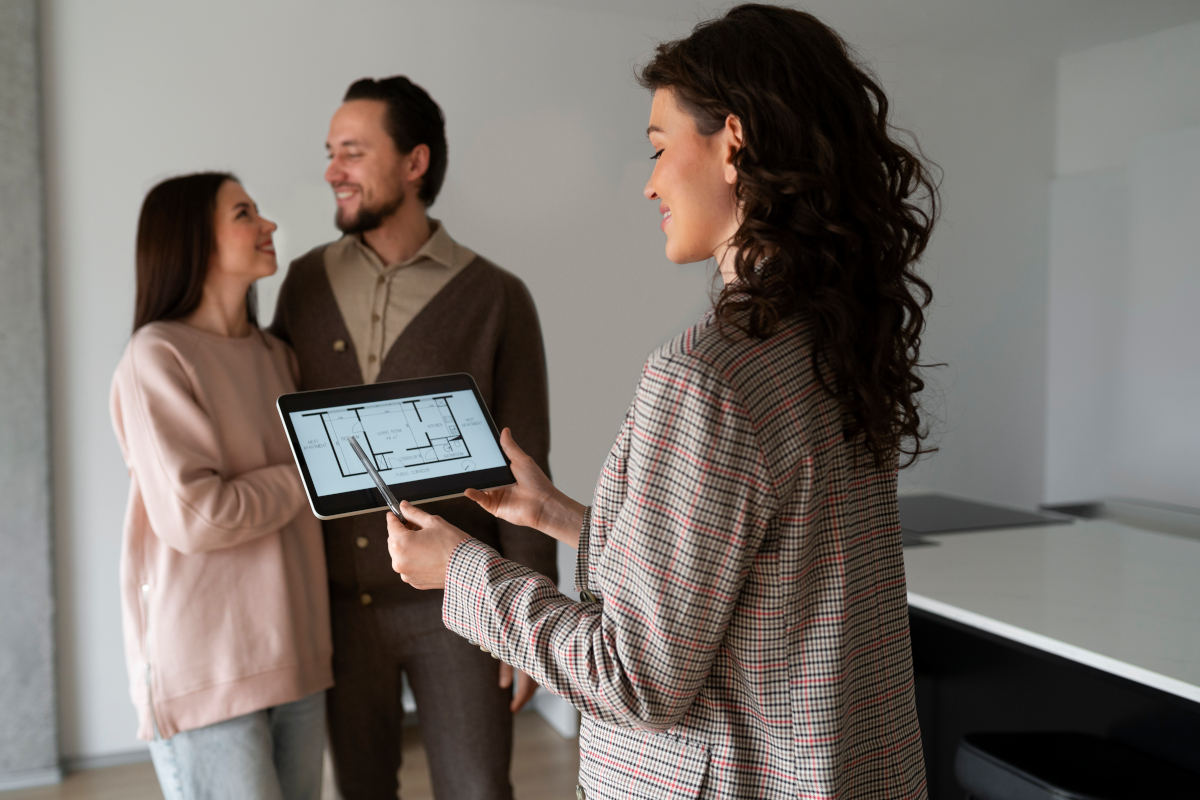 Maklerin mit Tablet präsentiert einem jungen Paar den Grundriss einer Wohnung