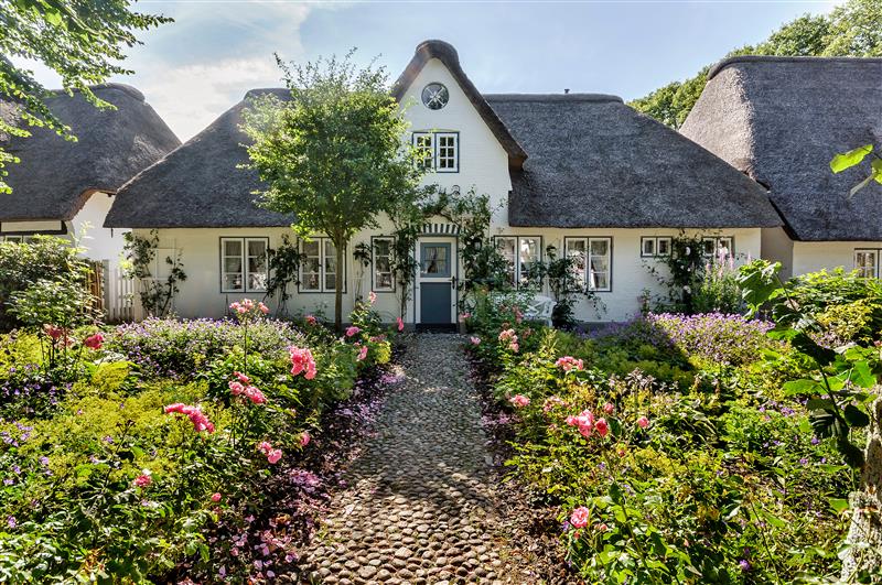 Bild eines Friesenhauses mit Reetdach und grünem Vorgarten