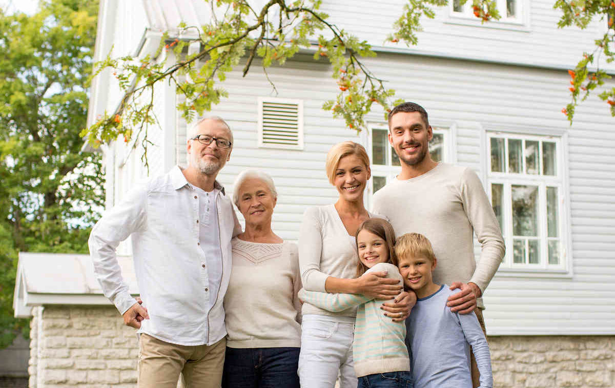 Großeltern, Eltern und Kinder stehen vor einem Haus - Symbolbild für Mehrgenerationenhäuser